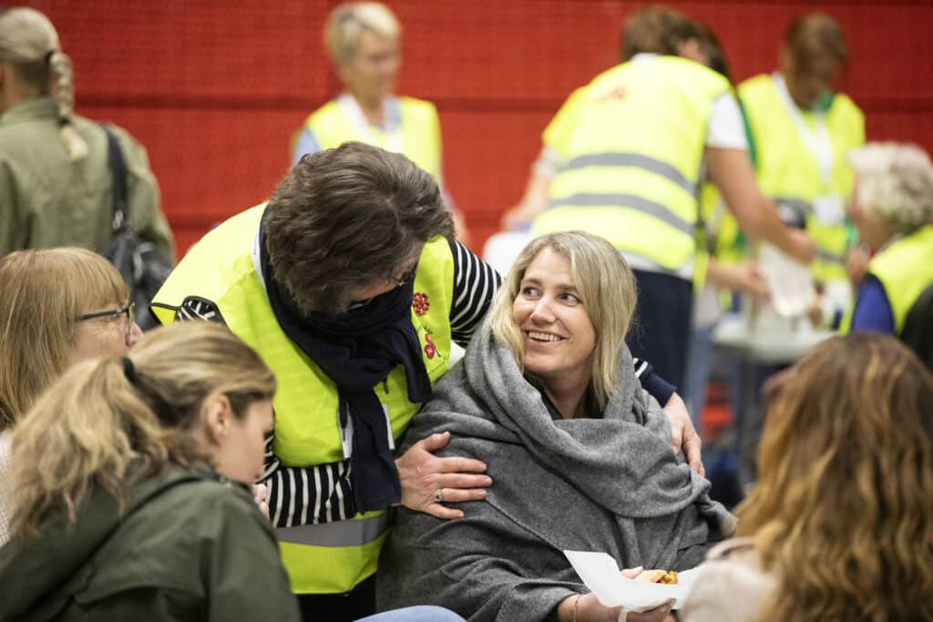 Kvinner holder rundt en annen kvinne som sitter med pledd på seg.